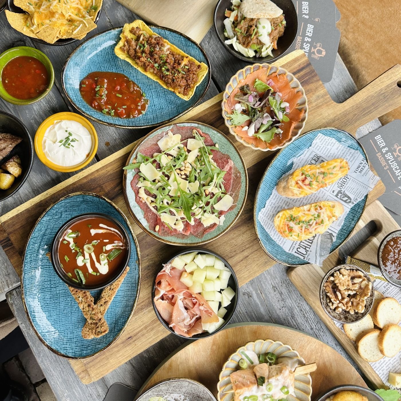 Tafel met tapas van bovenaf: carpaccio, soep, ham en dips